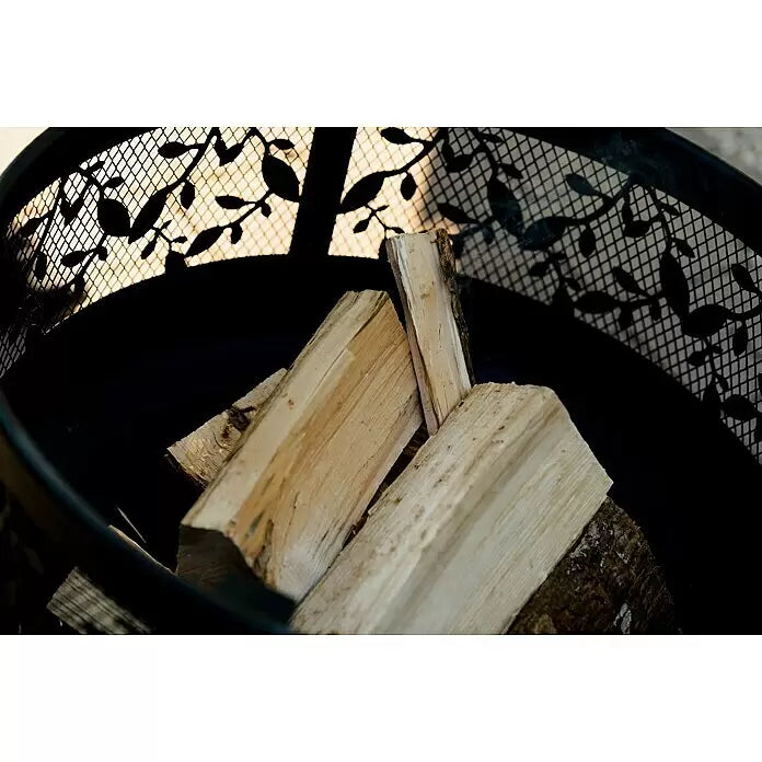 Fireland Kaminholz Raummeter - Laubholz, Länge Holzscheit: 25 cm - 33 cm - Schwarze Metall-Feuerschale mit dekorativem Gittermuster und Holzscheiten. Leichter Rauch sichtbar.